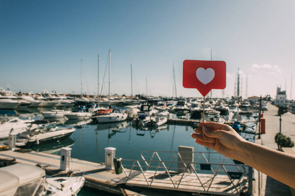 cropped view of woman holding red heart on stick as like near docked ships in mediterranean sea