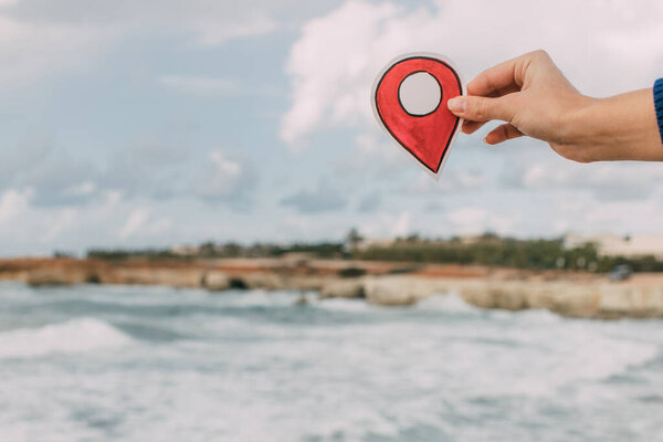 cropped view of woman holding red location paper near coastline of mediterranean sea in cyprus  