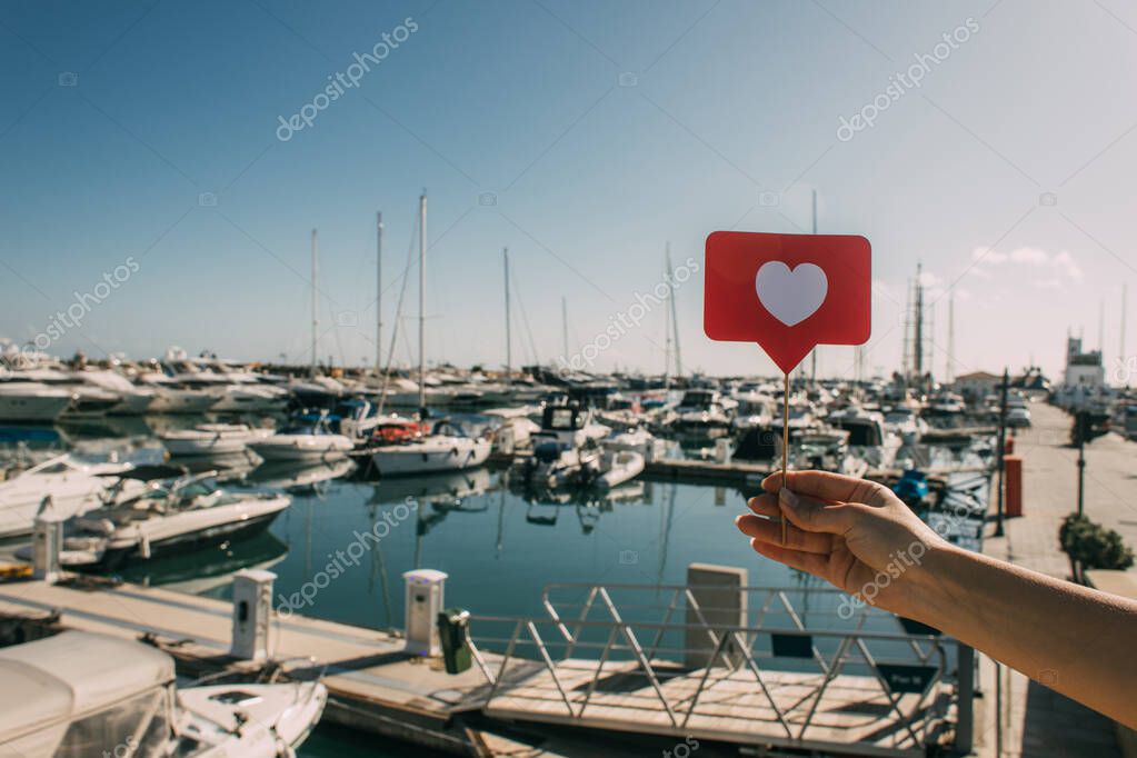 vista ritagliata della donna che tiene il cuore rosso sul bastone come vicino alle navi attraccate nel Mar Mediterraneo
