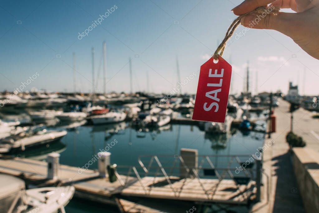 vista ritagliata di donna in possesso di etichetta rossa con la vendita di lettering vicino yacht attraccati nel mare Mediterraneo 