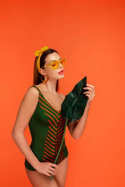 Vrouw Badpak Zonnebril Kijkend Naar Groen Blad Geïsoleerd Oranje — Stockfoto