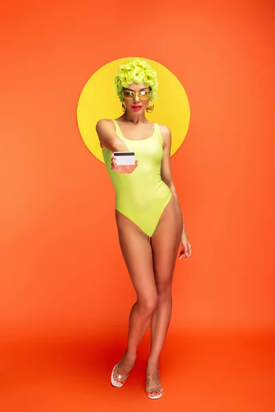 Девушка Шляпе Декоративными Цветами Показывает Кредитную Карту Желтым Кругом Позади — стоковое фото