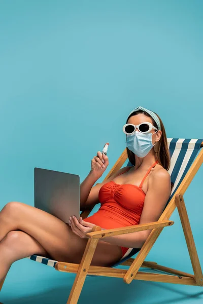 医療用マスクのフリーランサーとノートパソコンを示すボトルのハンドサニタイザーオンデッキチェア上の青 — ストック写真