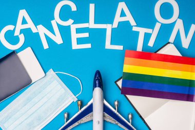 Top view of toy plane, passport near medical mask with lgbt flag and lettering cancellation on blue background clipart