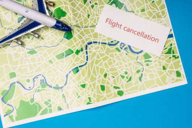 Top view of card with flight cancellation with toy plane on map isolated on blue  clipart