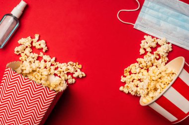 Top view of hand sanitizer, medical mask and buckets with popcorn on red surface  clipart