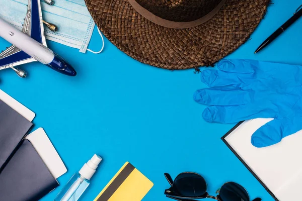 医療用マスクの近くのおもちゃの飛行機のトップビュー パスポートとラテックス手袋と太陽の帽子青の背景 — ストック写真