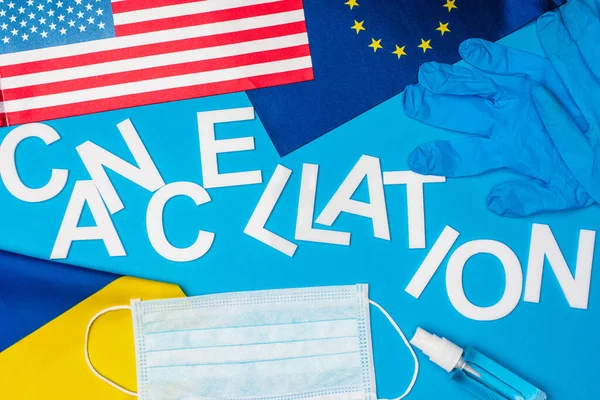 青い背景にウクライナ ヨーロッパの団結と文字のキャンセルや医療マスクの近くのアメリカの旗のトップビュー — ストック写真