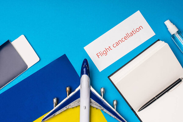 Вид сверху игрушечного самолета, карточка с отменой рейса, лежащая рядом с паспортом с авиабилетом и флагом России на синем фоне
