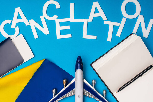 Вид сверху на отмененный полет рядом с игрушечным самолетом, паспорт с авиабилетом и флаг Украины на синем фоне
