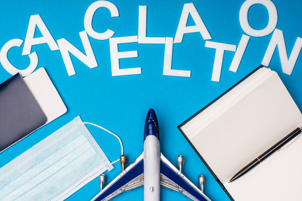 Top view of toy plane, medical mask with notebook and cancellation lettering on blue background