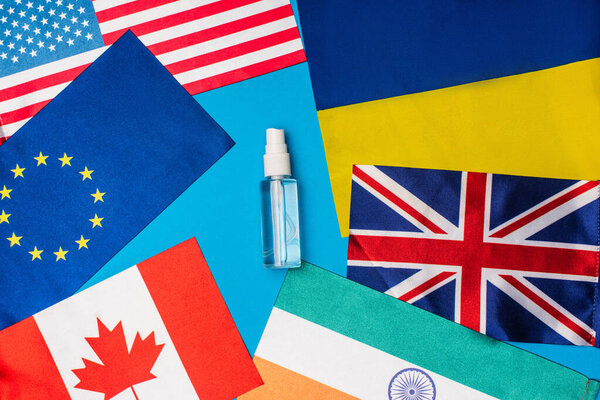 Top view of bottle of hand disanitizer near flags of countries on blue background
