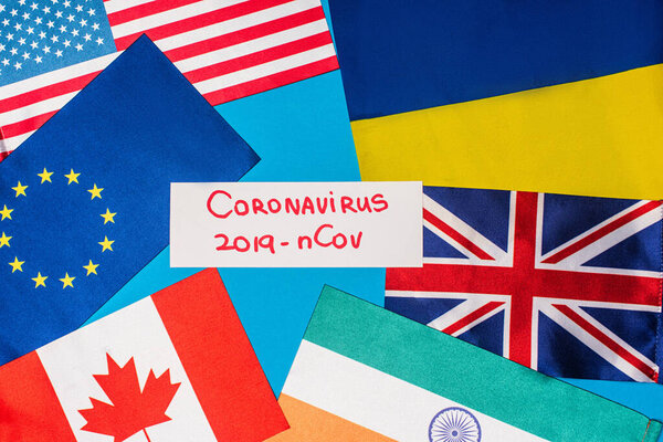 Top view of card with coronavirus 2019-nCov lettering near flags of countries on blue surface