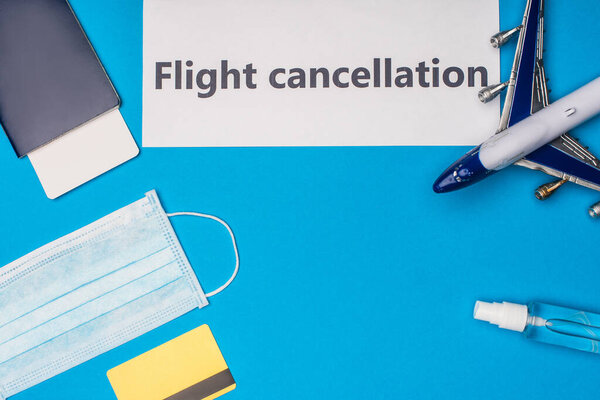 Top view of card with flight cancellation lettering, medical mask, credit card and toy airplane on blue background