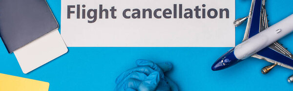 Вид сверху на врача возле игрушечного самолета, карточка с отметкой об отмене рейса и паспорт с авиабилетом на голубую поверхность, панорамный снимок
