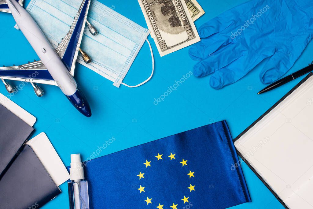 Top view of toy plane, medical mask with hand sanitizer and flag of european union on blue background