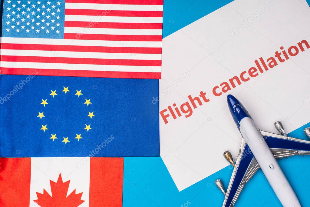 Top view of flags of canada, european union and america near toy plane with flight cancellation lettering on card on blue surface