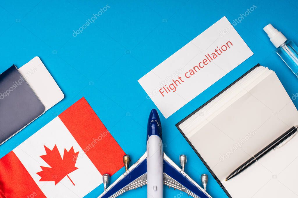 Top view of toy plane, card with flight cancellation lettering and flag of canada on blue background