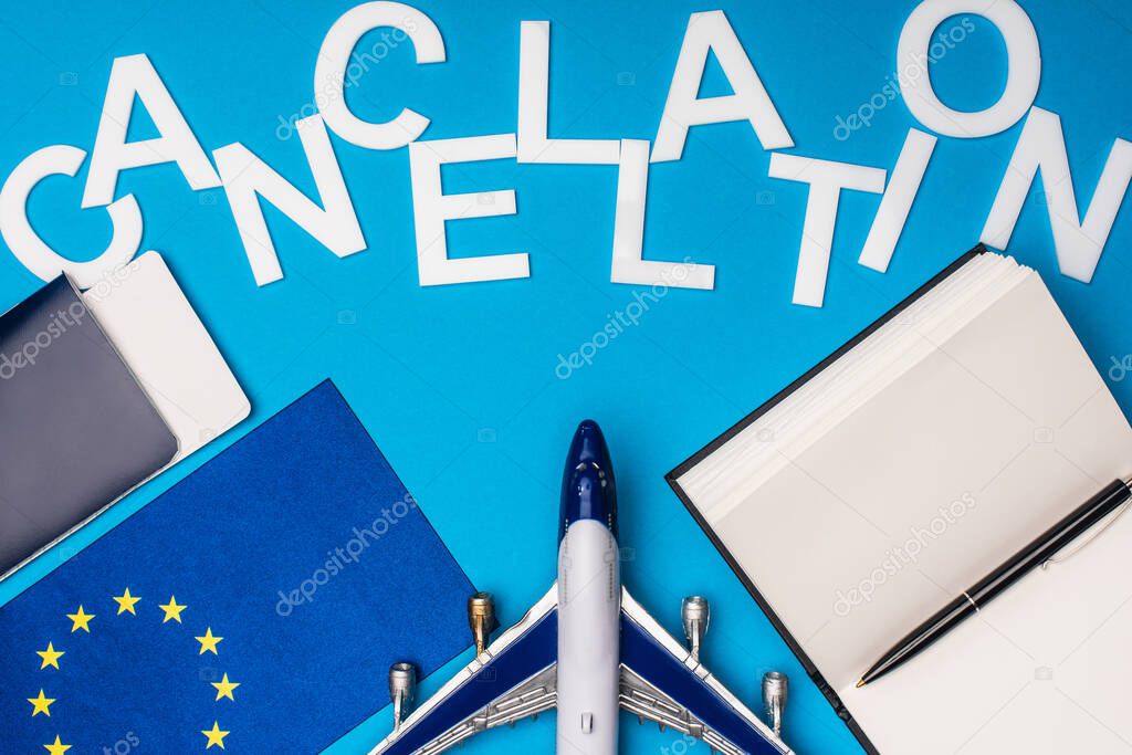 Top view of lettering cancellation near toy plane, flag of european unity and passport with air ticket on blue background