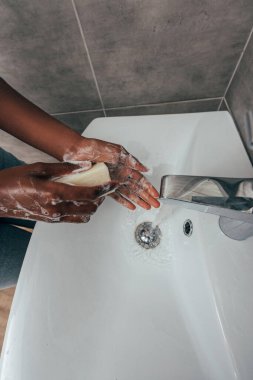 cropped view of african american girl washing hands with soap in bathroom clipart