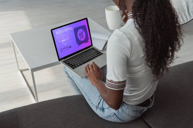 Ekranda en iyi alışveriş sitesi olan dizüstü bilgisayar kullanan Afro-Amerikan bir kızın yüksek açılı görüntüsü