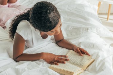 overhead view of young african american woman reading book in bed clipart