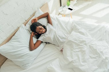 Yatakta yatarken gülümseyen neşeli, güzel Afrikalı Amerikalı kız manzarası