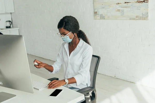 집에서 직장에 앉아서 의료용 마스크를 아프리카 미국인 프리랜서가 키보드에 살균제를 — 스톡 사진