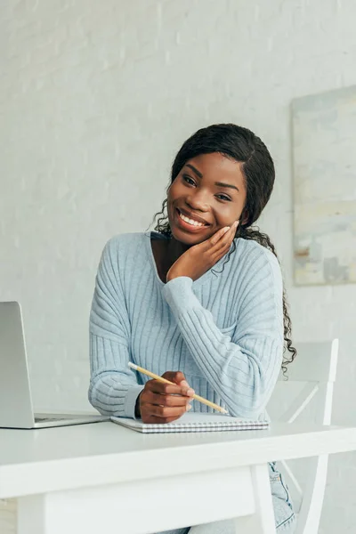 Feliz Afroamericano Freelancer Sonriendo Cámara Mientras Sostiene Lápiz Cerca Portátil —  Fotos de Stock