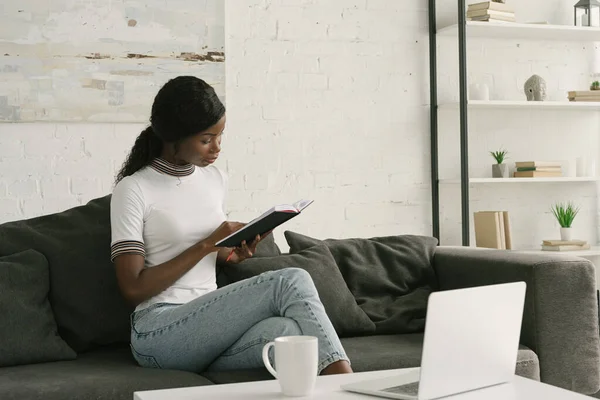 Young African American Freelancer Reading Notebook While Sitting Sofa Table — Stock Photo, Image