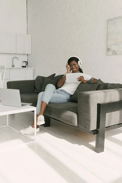 Cheerful African American Freelancer Wireless Headphones Sitting Sofa Holding Digital — Stock Photo, Image