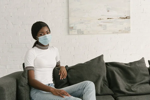 Pensive African American Girl Medical Mask Sitting Grey Sofa Home — Stock Photo, Image