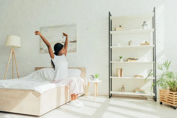 Afroamericana Chica Pijama Sentado Amplio Dormitorio Estiramiento Con Las Manos —  Fotos de Stock