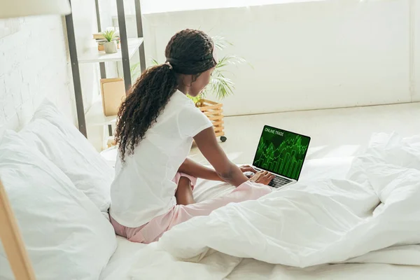 back view of young african american freelancer using laptop with online trade website on screen