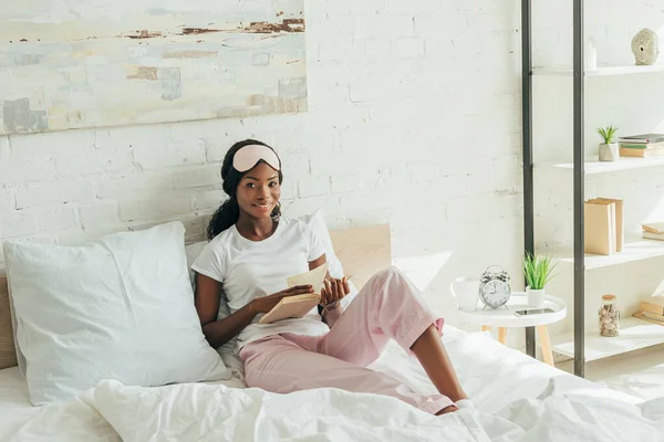 Sonriente Afroamericana Chica Con Máscara Sueño Frente Sentado Cama Sosteniendo — Foto de Stock