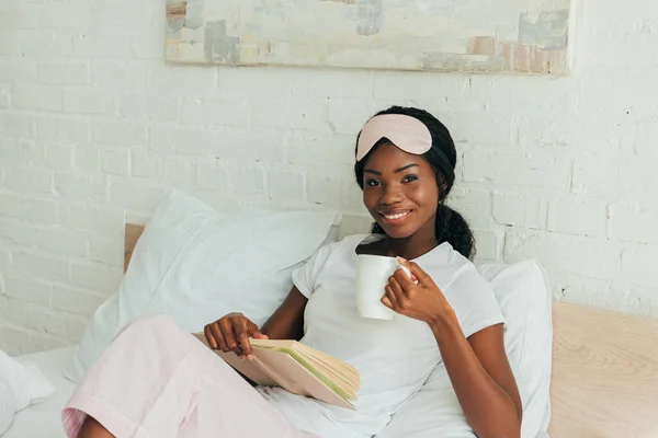 Szczęśliwy Afryki Dziewczyna Maską Snu Czole Siedzi Łóżku Trzymając Książkę — Zdjęcie stockowe