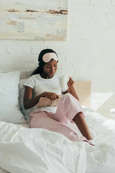 Alnında Uyku Maskesi Olan Afro Amerikalı Kız Yatakta Oturmuş Kitap — Stok fotoğraf