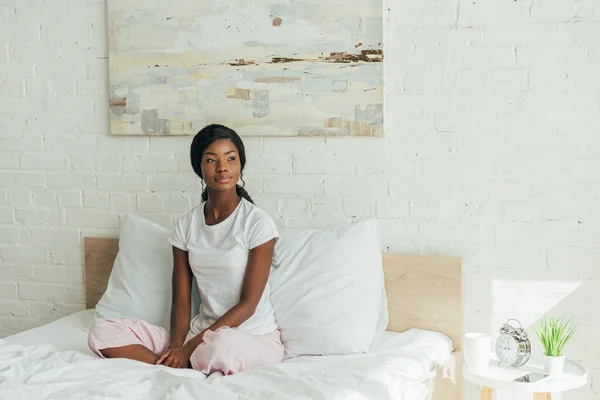 Αμερικανίδα Πιτζάμες Που Κάθεται Στο Κρεβάτι Σταυρωμένα Πόδια Και Κοιτάει — Φωτογραφία Αρχείου