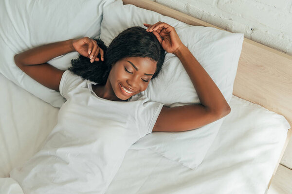 top view of happy, attractive african american girl smiling while lying in bed