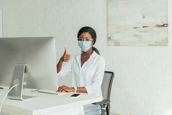 Young African American Freelancer Medical Mask Showing Thumb While Sitting — Stock Photo, Image