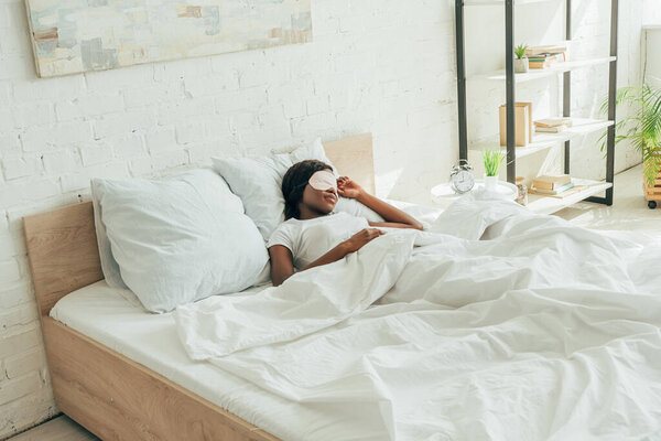 african american girl in sleep mask sleeping on white bedding in spacious bedroom
