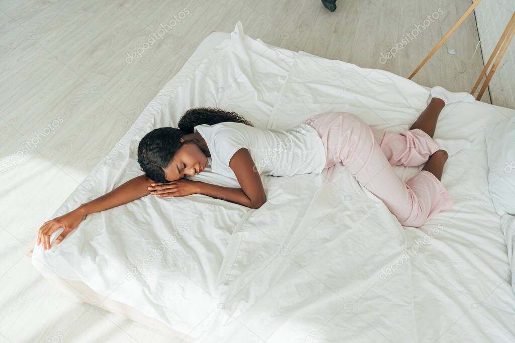 high angle view of african american girl in pajamas sleeping on white bedding