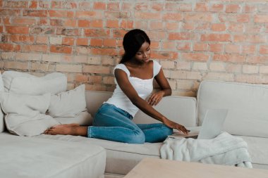 Oturma odasındaki kanepede dizüstü bilgisayarı olan Afrikalı Amerikalı serbest yazar. 