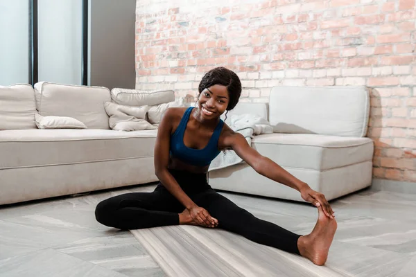 非裔美国女运动员面带微笑 看着镜头 躺在客厅的瑜伽垫上 — 图库照片