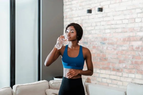 African american sportswoman drinking water in living room