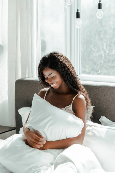 Mujer Afroamericana Sosteniendo Almohada Sonriendo Cama Dormitorio —  Fotos de Stock