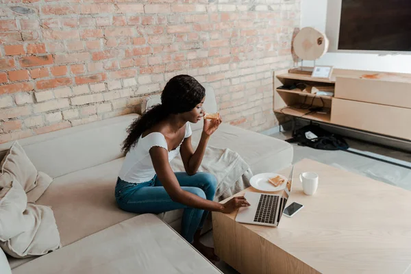 African American Freelancer Using Laptop Holding Toast Coffee Table Sofa — Stock Photo, Image