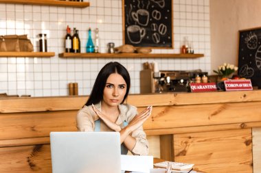 Kafe sahibi kameraya bakıyor ve masadaki dizüstü bilgisayarın, hesap makinesinin ve kağıtların yanında hiçbir işaret yok.