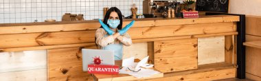 Medikal maskeli kafe sahibinin web sitesi başlığı, masada dizüstü bilgisayarlı, kağıtlı ve karantina yazılı bir tabela göstermiyor.