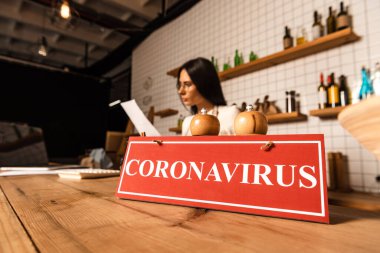 Kafe sahibinin seçici odak noktası Coronavirus harfleri ve masada tuz ve karabiber değirmenleri olan kartın yanındaki kağıda bakmak.